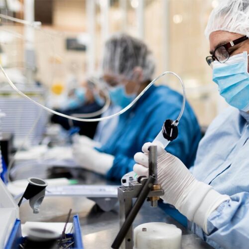 Medical device manufacturing technician assembling precision components in a cleanroom environment.