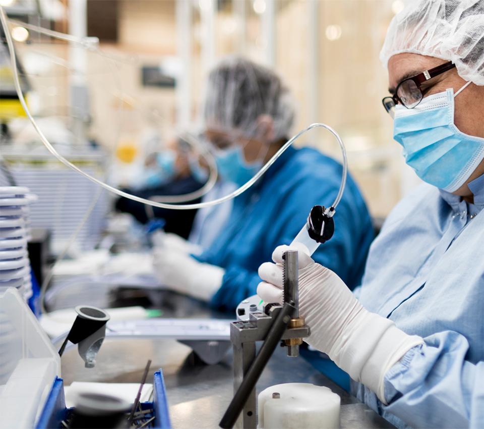 Medical device manufacturing technician assembling precision components in a cleanroom environment.