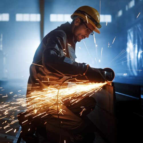 Industrial worker with sparks flying in dark setting.